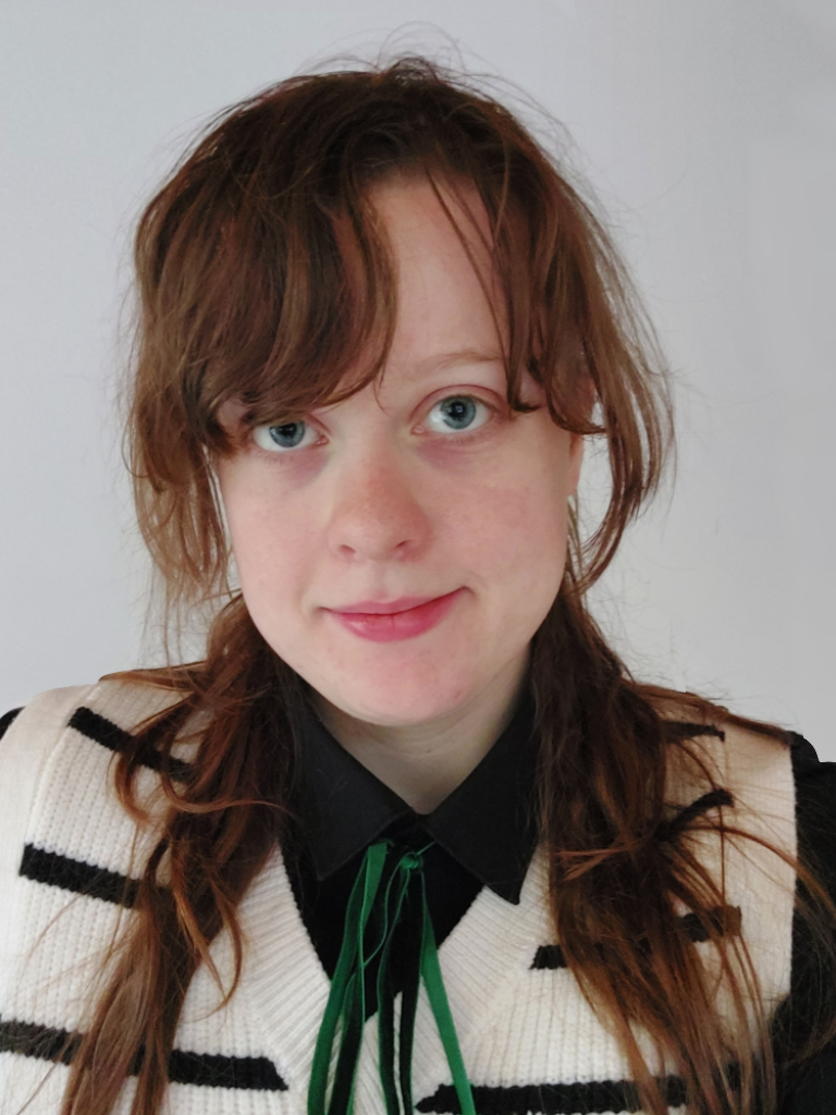 A picture of L Jordan wearing a white and black striped sweater vest over a black button-up shirt.