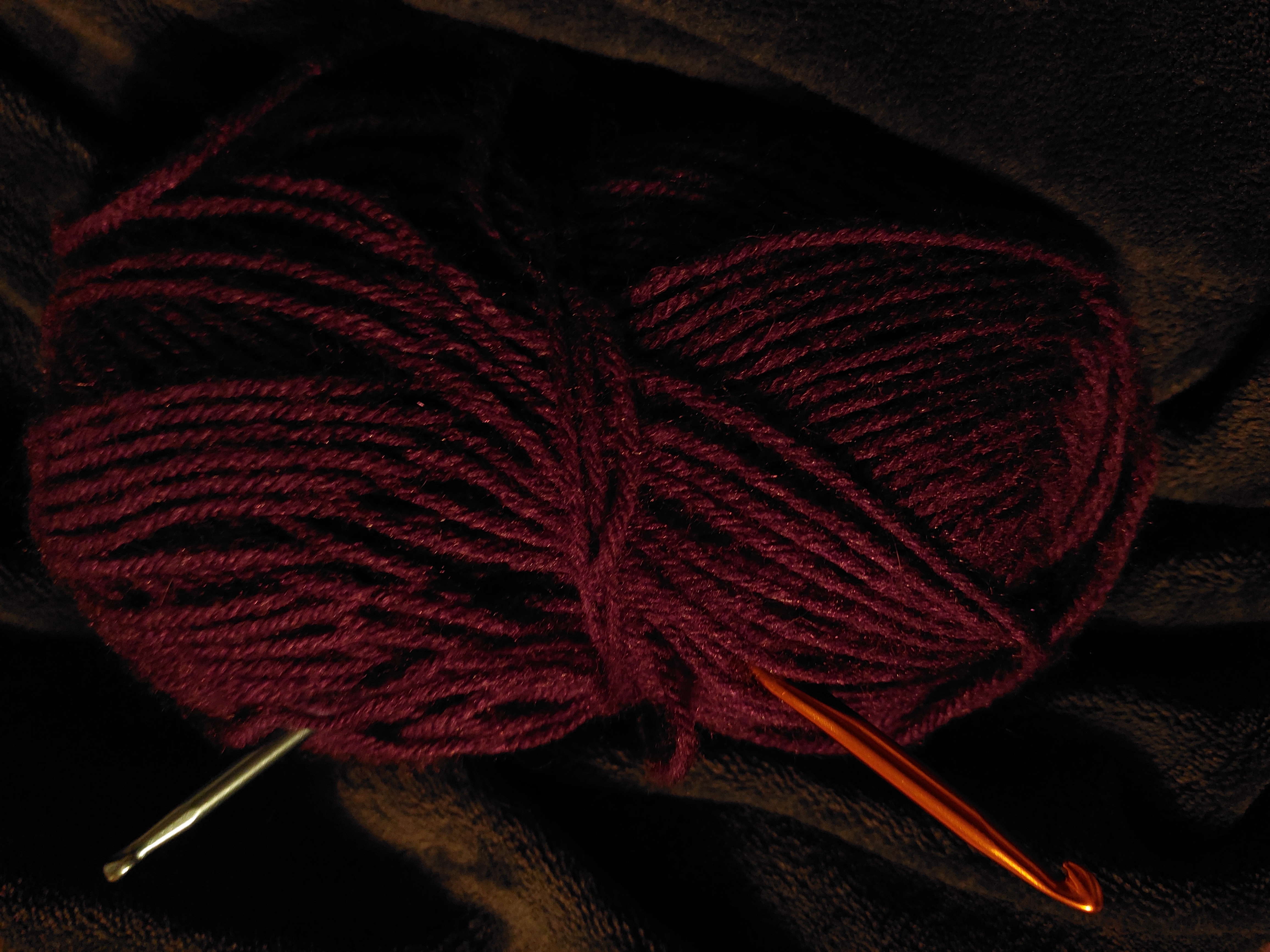 A purple ball of wool with two crochet hooks sticking out of it.